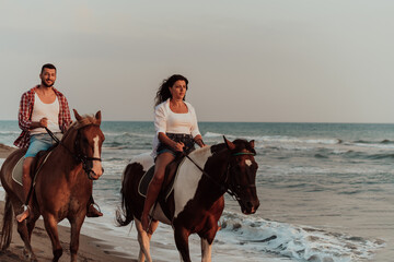 A loving couple in summer clothes riding a horse on a sandy beach at sunset. Sea and sunset in the background. Selective focus 