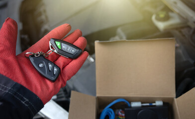 The hand of the master holds the keyfobs of the alarm system from the car.Installation of car theft...