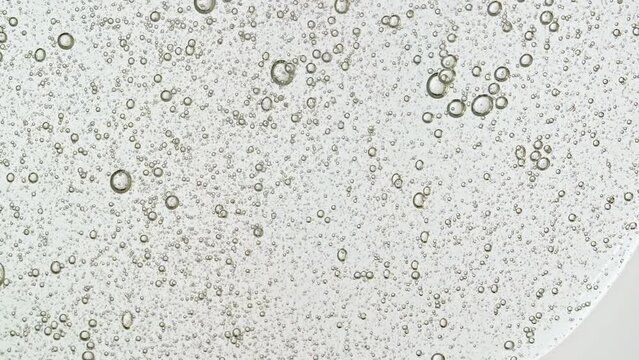 Transparent Cosmetic Gel Fluid With Molecule Bubbles Flowing On The Plain White Surface. Macro Shot of Natural Organic Cosmetics, Medicine. Production Close-up. Slow Motion. High quality 4k footage