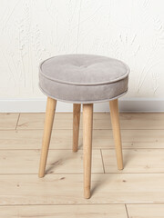 Round soft stool with wooden legs on white wall background. Upholstered furniture for home
