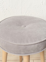 Round soft stool with wooden legs on white wall background. Upholstered furniture for home. Pouf closeup