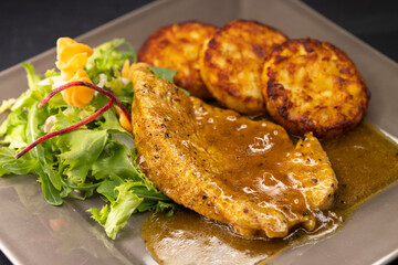 poultry meat with sauce served with hash browns and salad