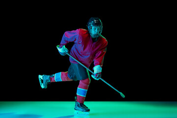 Counterattack. Professional male hockey player training in special uniform with helmet isolated over dark background in neon light