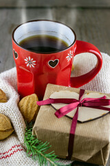Fototapeta na wymiar Close-up view of red cup of hot tea with Christmas fur-tree branches, nut cookies and gift box on old wooden background