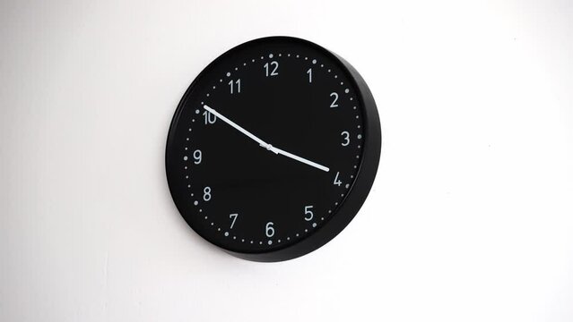 Time lapse of a black clock on a white wall. Minutes moving rapidly past 4pm.