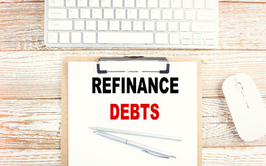REFINANCE DEBTS text on a clipboard with keyboard on wooden background
