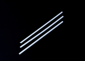 Disposable white plastic straws and black background.