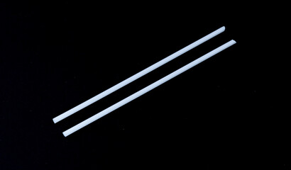 Disposable white plastic straws and black background.