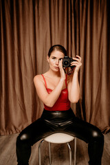 Party girl portrait. Young woman in red corset and black leather pants with photo camera. Sexy seductive brunette in red and black costume. Role play. Celebration and party. Having fun.