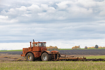Obraz premium big old model tractor plows the ground.