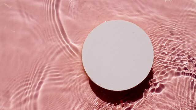 Empty white circle podium on transparent clear water texture with waves in sunlight. Slow motion of waves water on pink background. Sun and shadows. Video for design, advertising, products. 4k 
