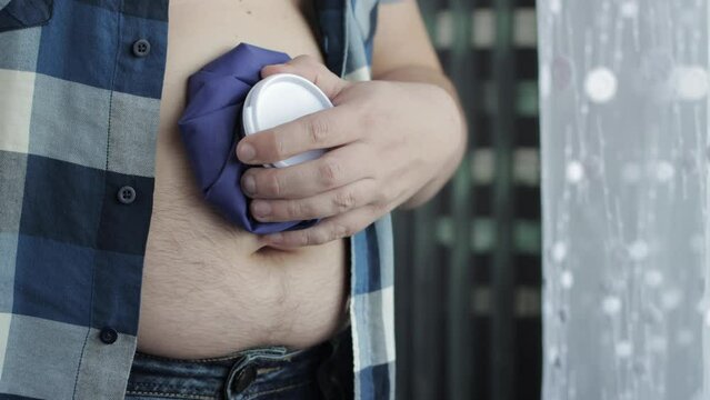 A man holds an ice bag near his stomach. Treatment of hematomas and stretching with cold. Anesthesia, close-up