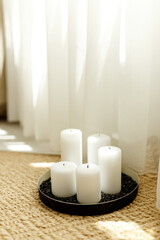 Fototapeta na wymiar Beautiful burning candle on floor in room. Natural floor cover, window curtains