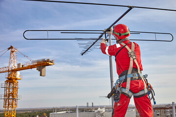 A specialist repairs an antenna on the roof. Rope access