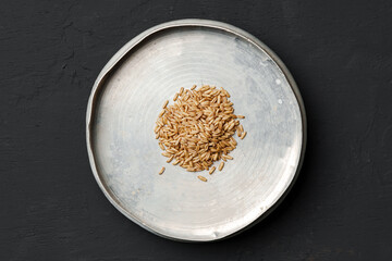 Concept of a global food crisis caused by hunger due to lack of grain. Plate with small amount of grain on plate on black background