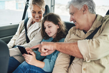 Child, grandparents and phone on road trip in car backseat streaming movie, elearning or helping with education game. Child, man and woman uber happy on travel journey and checking destination online