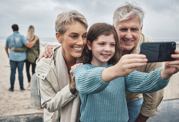 Phone, selfie and grandparents with a child at the beach while on family adventure, journey or...