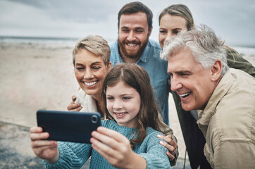 Fototapeta premium Family, selfie and girl with phone on beach for holiday, vacation or journey together by ocean. Group, mom and dad with child, grandparents and smartphone for photo in winter with smile by sea