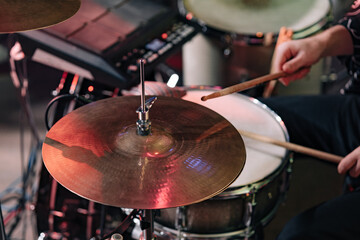 Fototapeta na wymiar Drummer playing drum sticks on a snare drum on black background. Hi-hat close-up of plates with drumsticks on a background of colored lanterns.