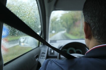 Driver with fastened seatbelt sitting in his car, seen from behind, on a rainy day