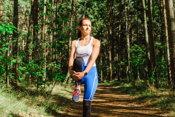 Young caucasian woman runner stretching legs before running in the summer park. Healthy workout woman jogging outdoors.