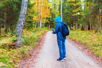 Man hiker lost in a autumn forest and search a mobile network on a hone.Tourist looking for a cellular connection on a hike.Full lenght hiker stand on the road.Travel Technology concept.