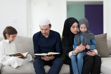 Traditional muslim family parents with children reading Quran and praying together on the sofa before iftar dinner during a ramadan feast at home