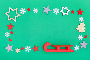Frame from red sleigh, snowflakes and wooden stars on a green background. Christmas and new year concept. Copy space, background.
