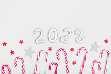 The inscription 2023, candy canes and wooden stars on a gray background. Christmas and New Year concept. Copy space.