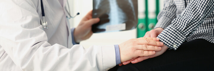 Qualified male doctor hold x ray scan of patients lungs and talk to client