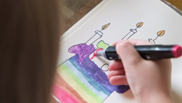 Child draws cake with candles with felt pen on paper. Girl enjoys painting process. Little girl painting. Close-up in 4K, UHD