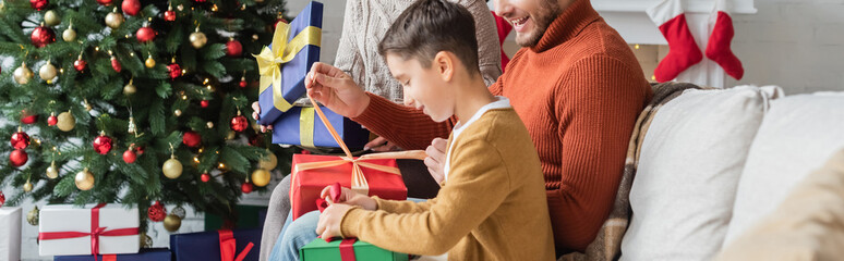 kid packing gift box near parents and christmas tree at home, banner