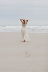 Fototapeta na wymiar A woman in a long romantic chiffon dress strolls along a beach by herself