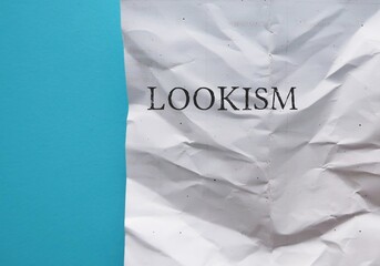 On copy space blue background, crumpled paper with text LOOKISM - discrimination treatment of...