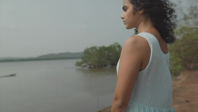 Slow motion panning shot of a beautiful fashionable woman dressed in a baby blue top looking pensively across the lake