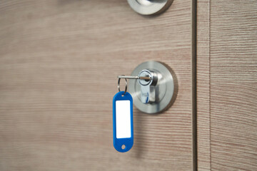 A key with a blank keychain in the lock of a wooden door close up. High quality photo