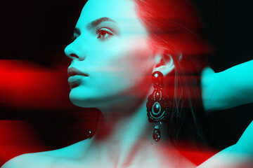 Beautiful and sexy looking woman with fancy earrings with gemstones studio portrait in RGB color split. RGB effect make reflection of model face in red and blue colors. Abstract and futuristic style