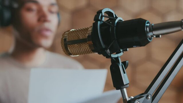Close-up professional microphone for audio recording of announcer or radio presenter and blurred man reading text from sheets of paper writing down new voice book or voicing movie character