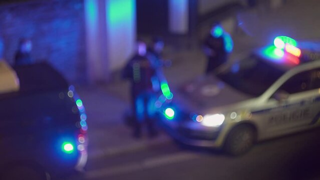 Blinking police beacon on cop car and group of officers around, blurry night bokeh view
