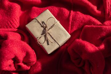 A gift in craft packaging with a sprig of viburnum against the background of a red sweater. Holiday gift. Christmas. New Year. Birthday. Valentine's Day. Holiday postcard.