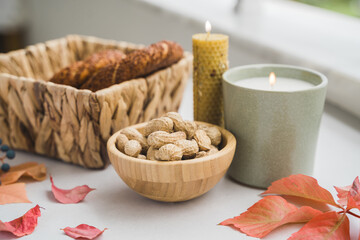 Fototapeta na wymiar Still life candle flame, peanut, fallen leaves, wicker basket, bagel on a table, home decor in a cozy house. Autumn weekend concept 