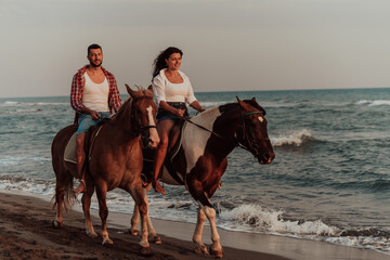 A loving couple in summer clothes riding a horse on a sandy beach at sunset. Sea and sunset in the background. Selective focus 