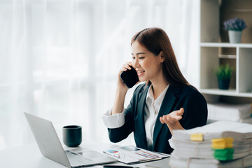 Obraz premium Asian businesswoman talking on phone, using laptop, looking at screen, entrepreneur manager consulting client by call, looking at computer screen, discussing project, reading information