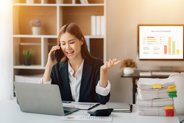 Asian businesswoman talking on phone, using laptop, looking at screen, entrepreneur manager consulting client by call, looking at computer screen, discussing project, reading information