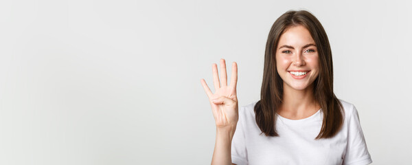 Fototapeta na wymiar Close-up of cheerful attractive young woman smiling, showing four fingers, white background