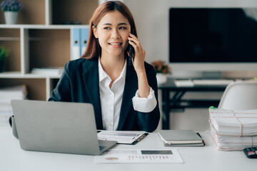 Asian businesswoman talking on phone, using laptop, looking at screen, entrepreneur manager consulting client by call, looking at computer screen, discussing project, reading information