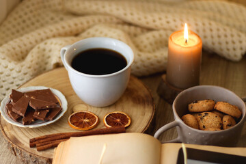 Obraz na płótnie Canvas Bowl of cookies, cup of tea or coffee, chocolate, spices, knitted blanket, books, glasses and candle on the table. Cozy hygge atmosphere at home. Selective focus.