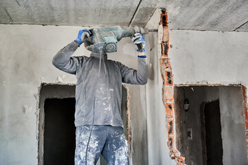 Strong repairman working with heavy special tool for destroying walls. Side view of builder with...