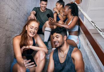 Obraz premium Fitness, phone and group of friends on stairs networking on social media together after gym workout. Happy, smile and sports people sitting and watching funny comic videos on internet with smartphone