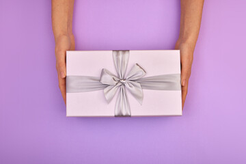 Hands holding blue gift box pink background. Hands give turquoise gift box with a card and a bow on...